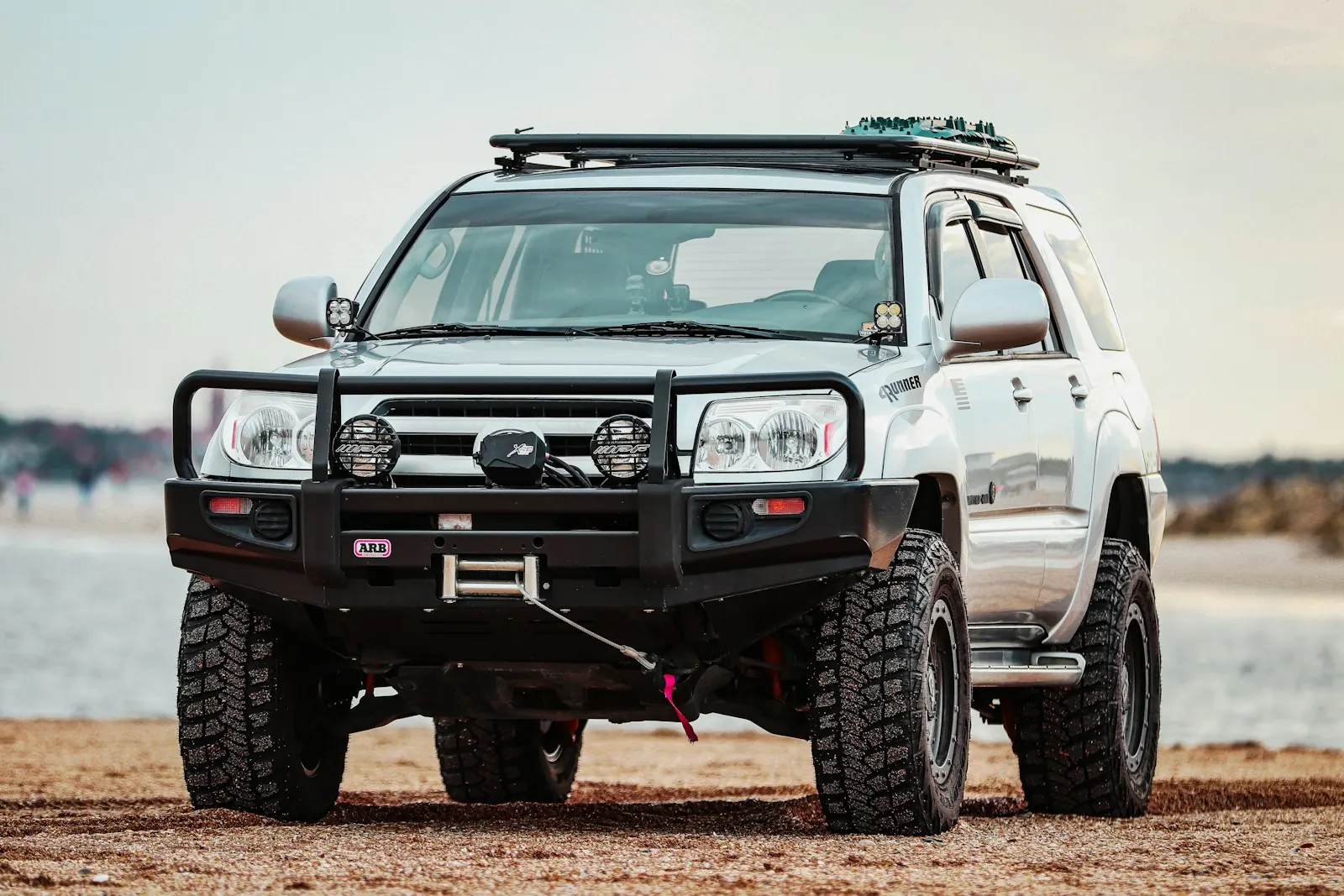 Silver SUV with a steel front bumper, winch, auxiliary lights and roof rack parked on a beach