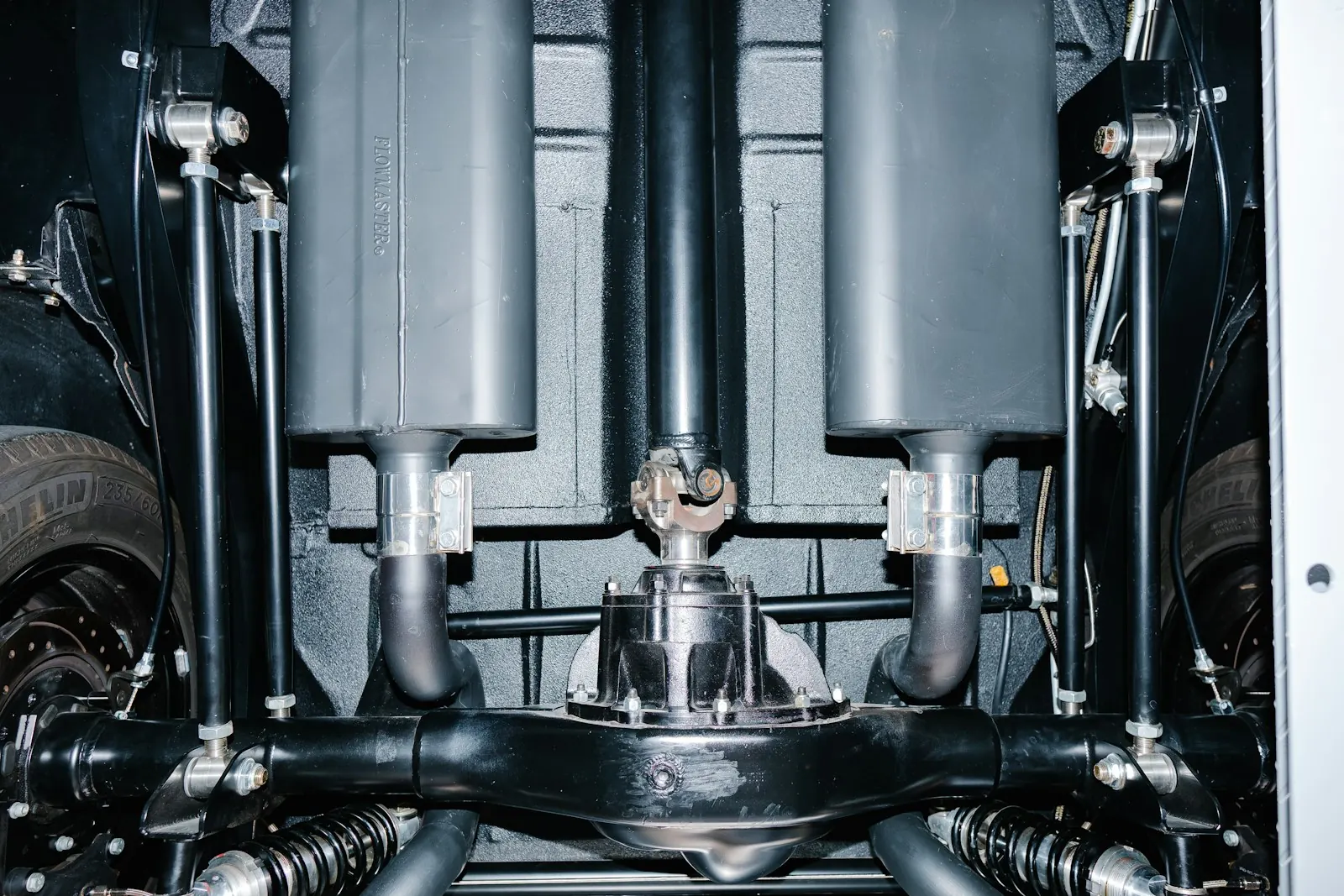 Underside view of a driveshaft and U-joint running into a rear differential between two mufflers